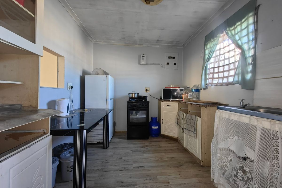 A functional kitchen space featuring laminate flooring, built-in cabinetry, a gas stove, and a sink, requiring some cosmetic updates to improve its overall condition.