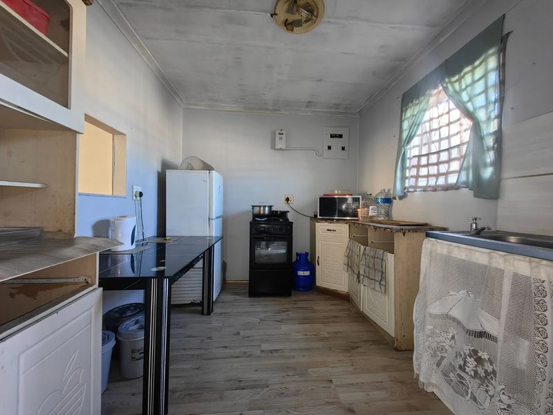 A functional kitchen space featuring laminate flooring, built-in cabinetry, a gas stove, and a sink, requiring some cosmetic updates to improve its overall condition.