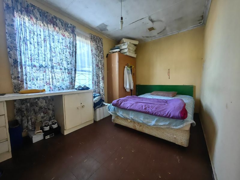 A bedroom featuring built-in cabinetry and a desk, currently showing significant signs of wear including ceiling damage and dated finishes.