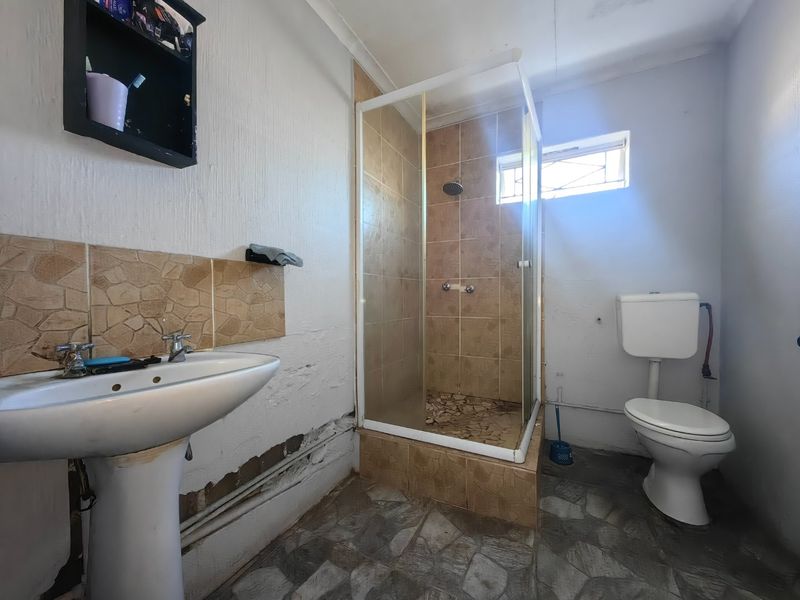 A functional bathroom featuring a pedestal basin, a corner shower enclosure, and a standard toilet, requiring cosmetic updates and wall repairs.