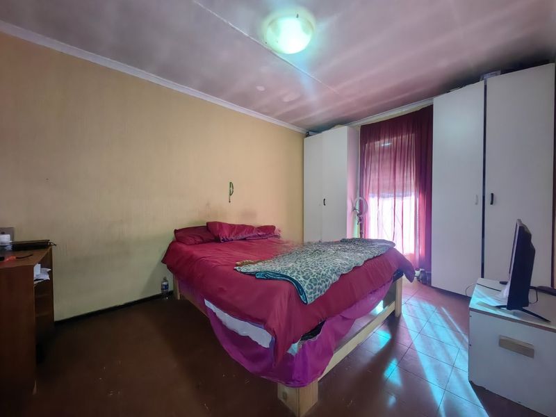 A bedroom featuring built-in cupboards, tiled flooring, and a ceiling light fixture. The room requires cosmetic updates to improve its overall condition.