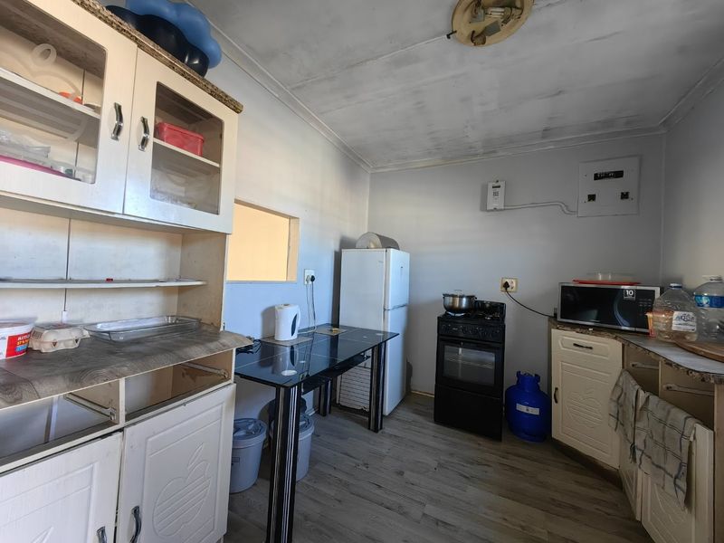 A functional kitchen space featuring built-in cabinetry, a gas stove, and laminate flooring, currently requiring cosmetic updates and ceiling repairs.