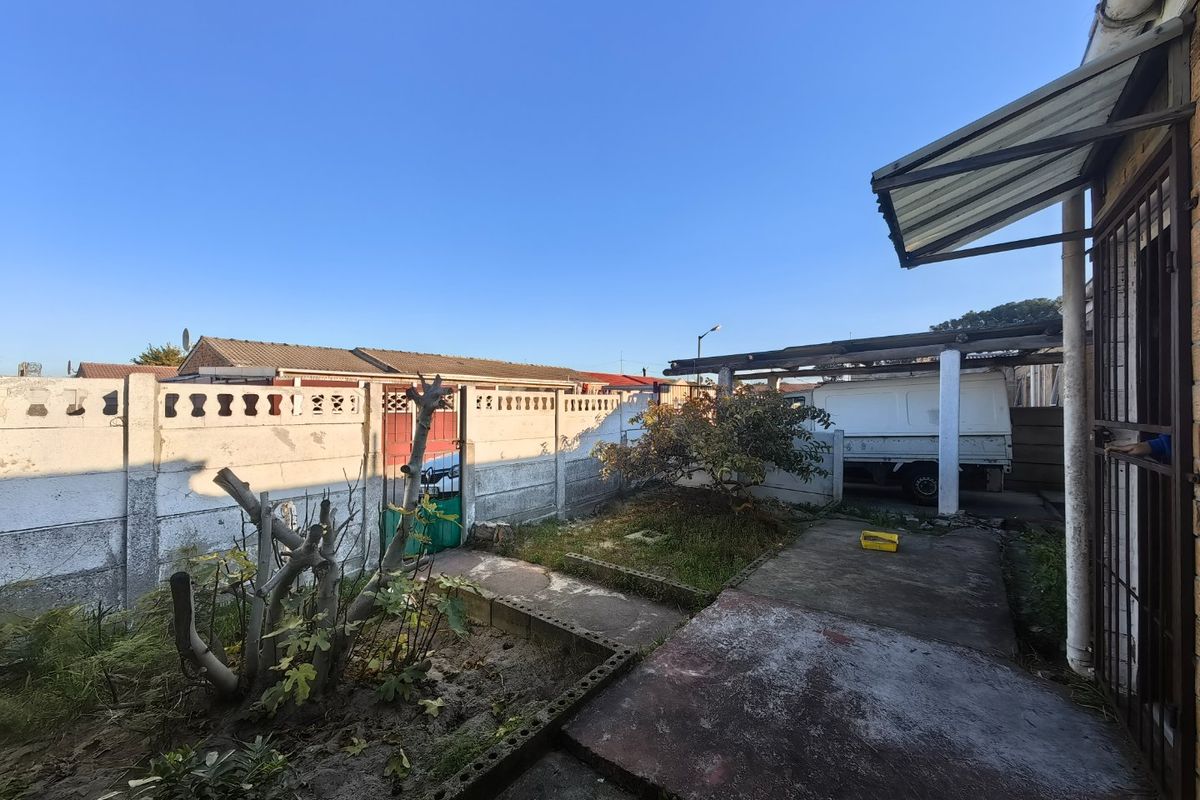 Rear exterior area featuring a concrete patio, covered carport structure, and precast concrete boundary walling in need of maintenance.