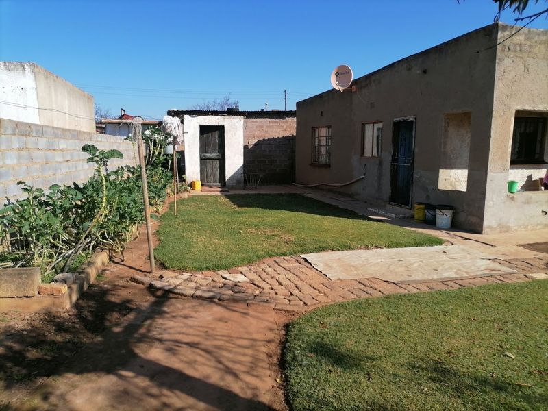 Rear exterior view of the property featuring a lawn, paved walkway, boundary wall, and a small outbuilding.