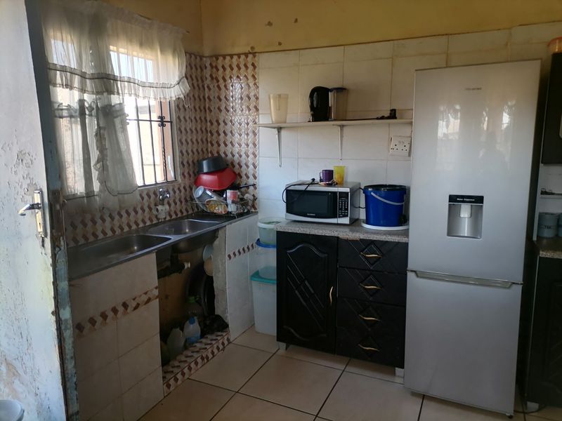 A compact kitchen featuring a double bowl sink, tiled splashback, and built-in cabinetry, currently requiring cosmetic updates and repairs to wall finishes.