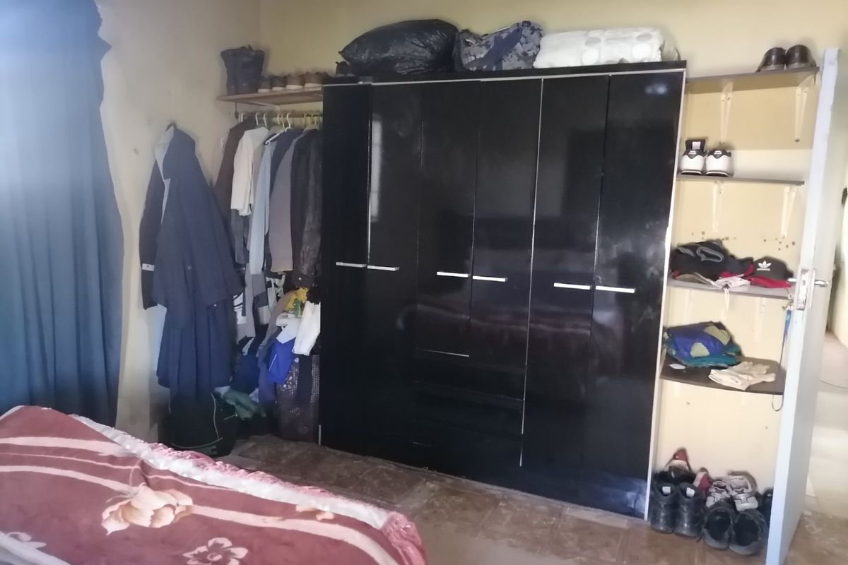 A bedroom featuring a large black built-in wardrobe, open shelving units, and tiled flooring, requiring cosmetic updates to improve the overall aesthetic.