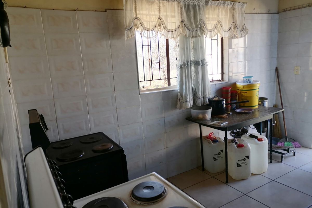 A functional kitchen featuring tiled walls and flooring, equipped with an electric stove and security bars on the window.
