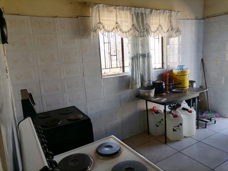 A functional kitchen featuring tiled walls and flooring, equipped with an electric stove and security bars on the window.