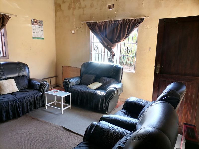 A living room space featuring security bars on the windows and a timber door, currently requiring significant wall repairs and cosmetic updates.