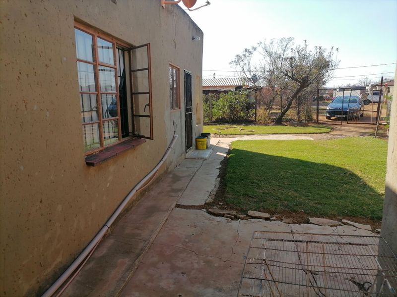 Rear exterior view of the property featuring a concrete patio area, lawn, and steel-framed windows.