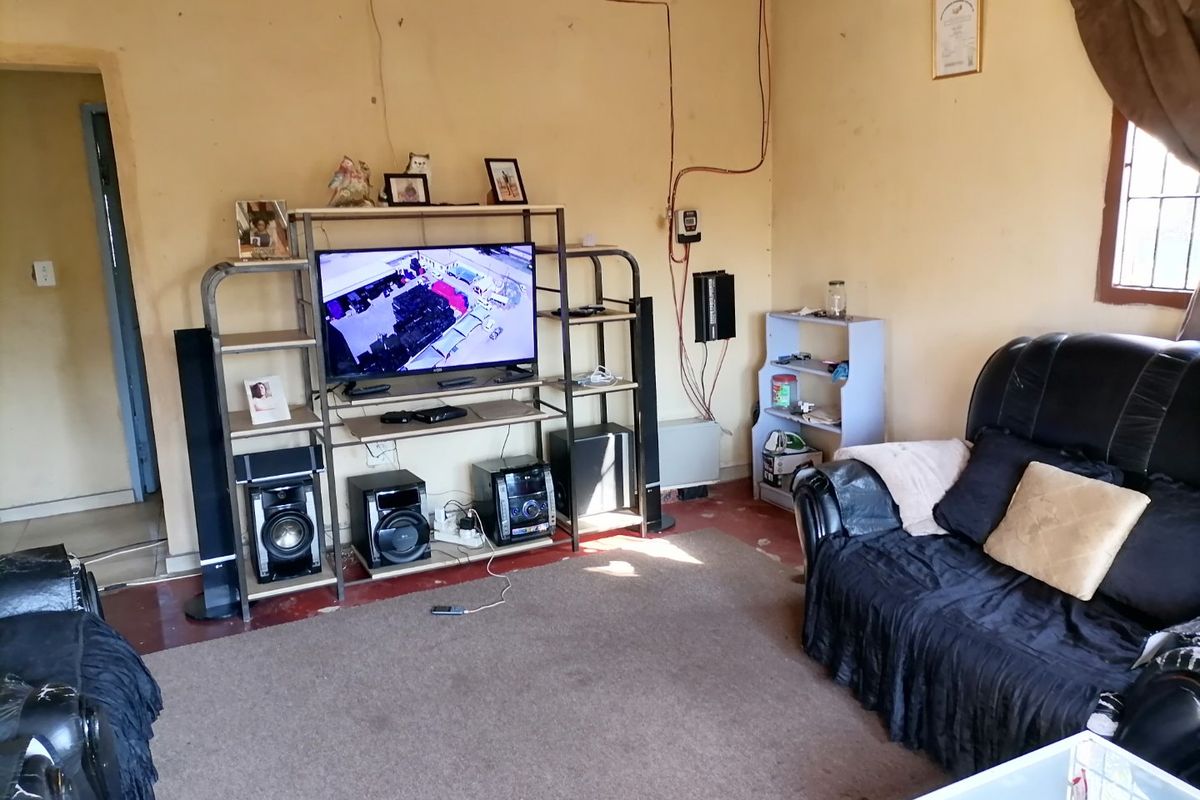 A living room featuring exposed electrical wiring and a window with security bars, requiring cosmetic updates to improve the overall aesthetic and finish.