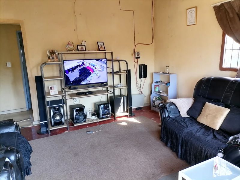A living room featuring exposed electrical wiring and a window with security bars, requiring cosmetic updates to improve the overall aesthetic and finish.