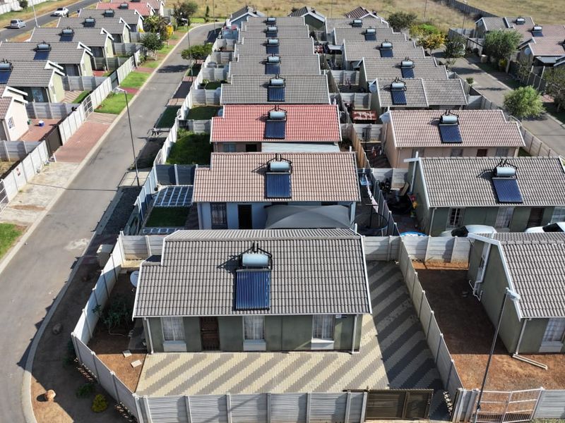 Aerial view of a residential estate featuring multiple detached houses with tiled roofs, solar water heating systems, and paved driveways.