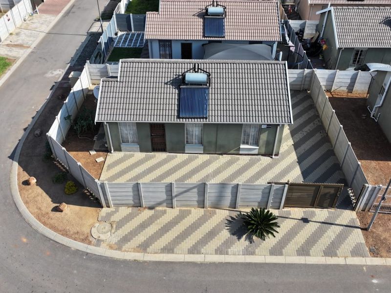 Aerial view of a residential property featuring a tiled roof with a solar water heater, paved driveway, and secure precast concrete boundary walling.