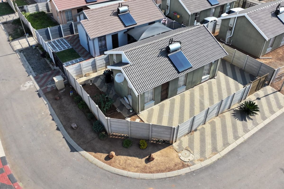 Aerial view of a residential property featuring a tiled roof with a solar water heater, paved driveway, and secure precast concrete boundary walls.