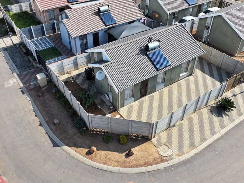 Aerial view of a residential property featuring a tiled roof with a solar water heater, paved driveway, and secure precast concrete boundary walls.
