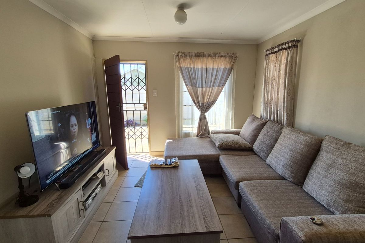 A functional living room featuring tiled flooring, a security gate at the entrance, and neutral wall finishes, providing a comfortable and practical living space.