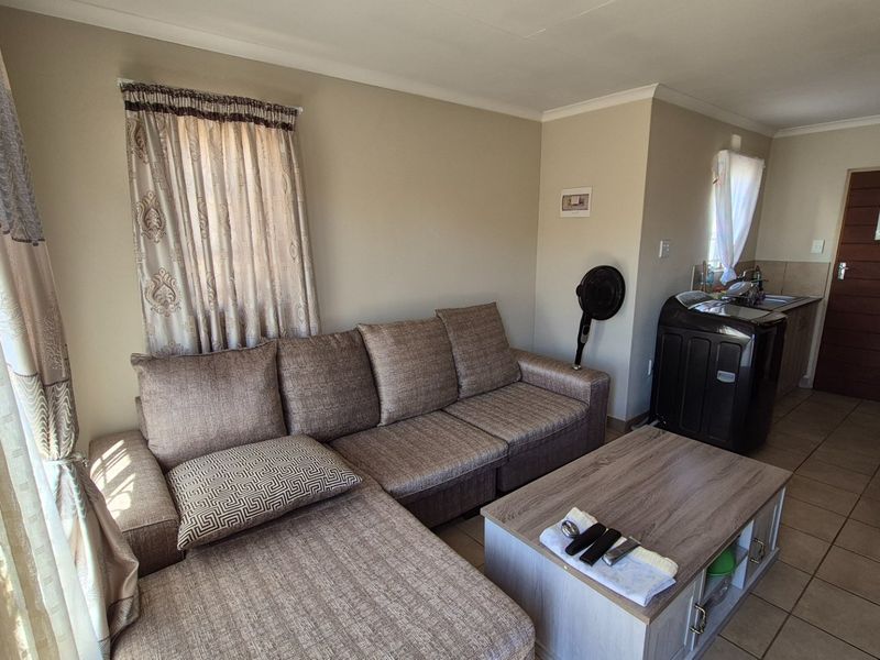 Open-plan living area featuring tiled flooring and a compact kitchen corner with built-in cabinetry and sink.