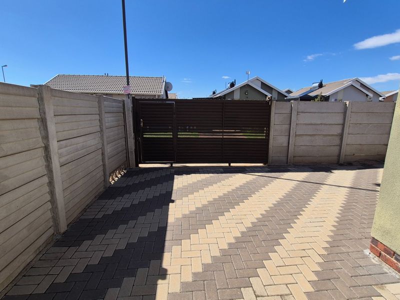 A secure rear courtyard area featuring a paved driveway, precast concrete boundary walls, and a metal access gate.