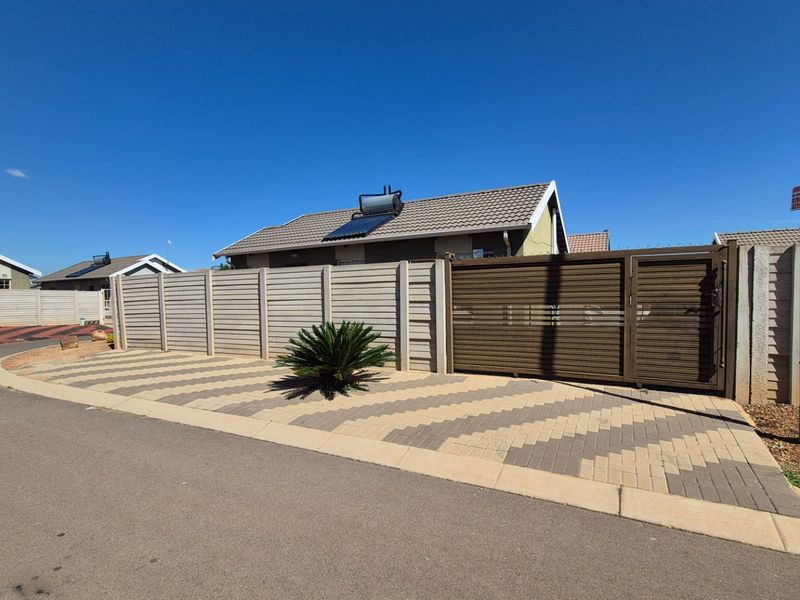 Front exterior view of the property featuring a paved driveway, secure sliding gate, precast boundary wall, and a roof-mounted solar water heating system.