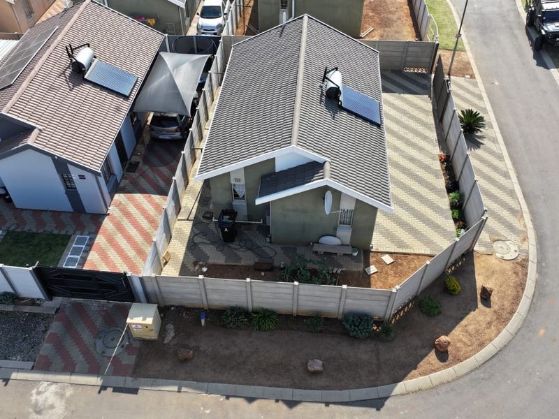 Aerial view of a residential property featuring a tiled roof with solar water heating, paved driveway, and secure perimeter walling.
