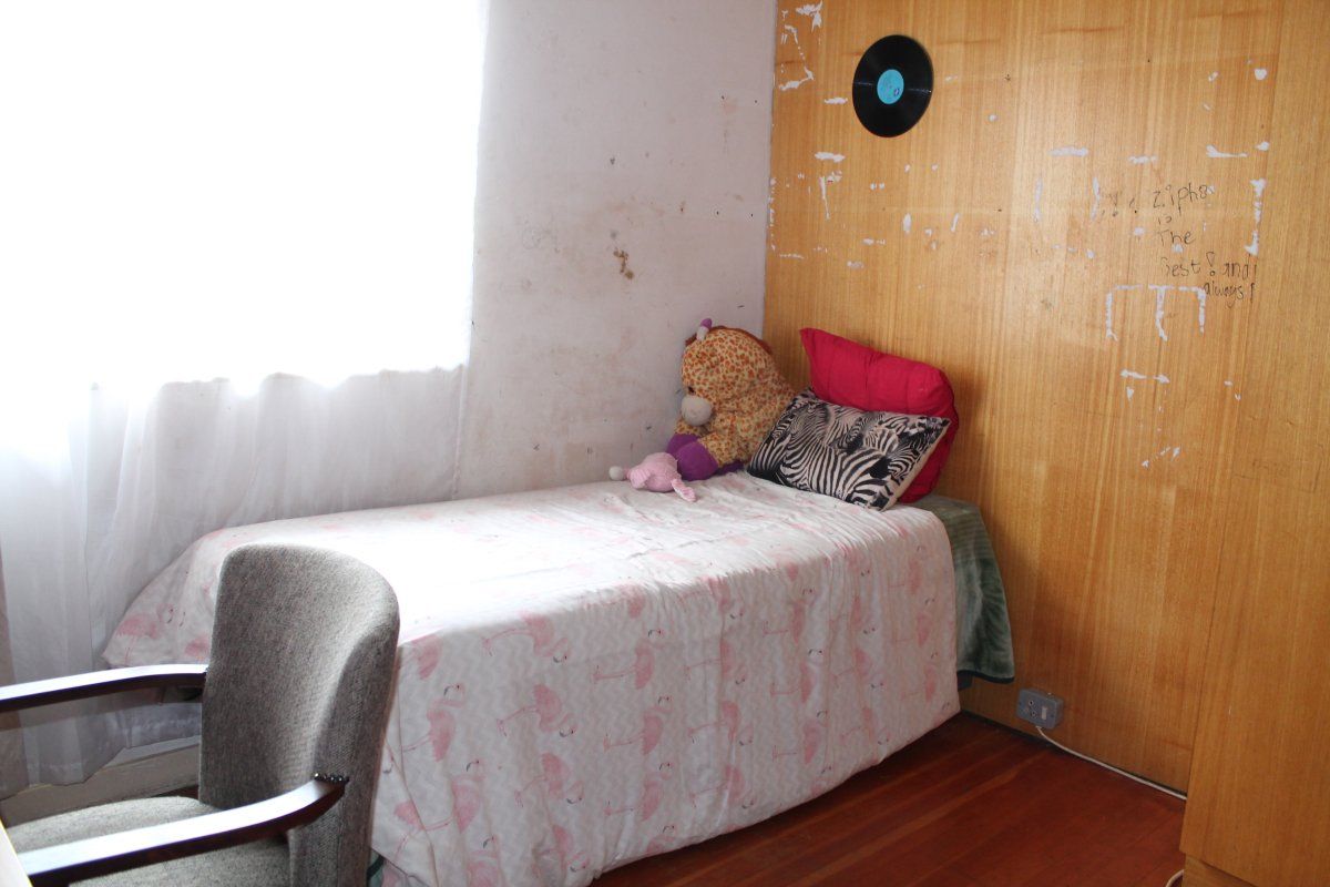A bedroom featuring hardwood flooring and built-in wooden wardrobe cabinetry, currently requiring wall repairs and cosmetic updates to improve the overall condition.