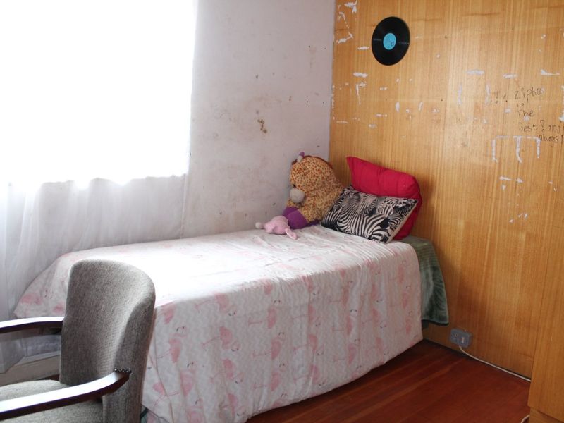 A bedroom featuring hardwood flooring and built-in wooden wardrobe cabinetry, currently requiring wall repairs and cosmetic updates to improve the overall condition.