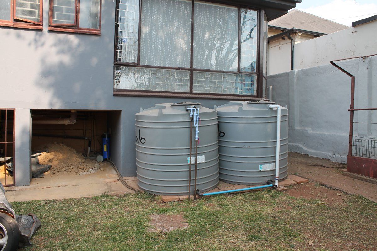Rear exterior view featuring two large grey water storage tanks connected to the property plumbing system, situated against a boundary wall.