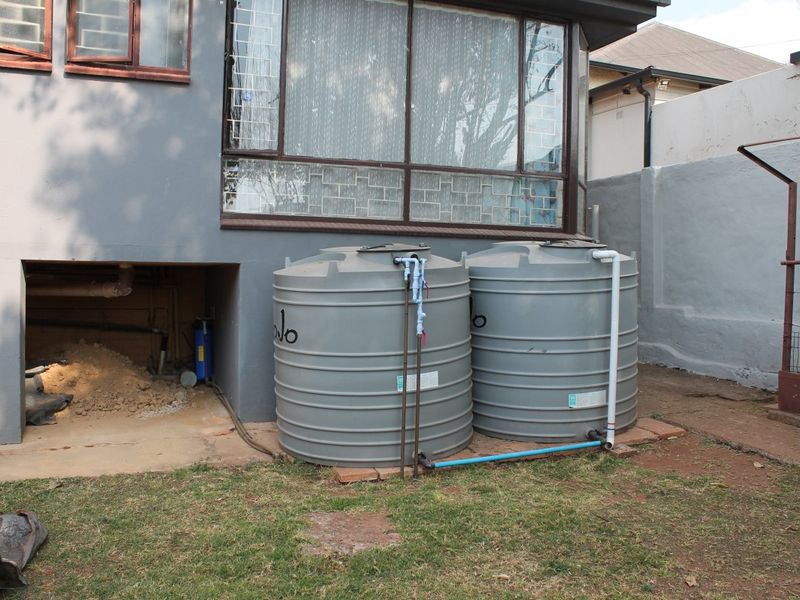 Rear exterior view featuring two large grey water storage tanks connected to the property plumbing system, situated against a boundary wall.