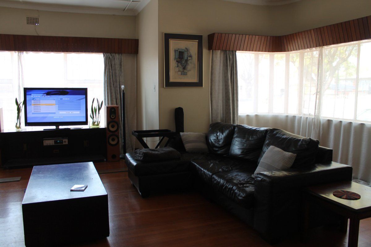 A living room featuring hardwood flooring, a large bay window with timber pelmets, and classic cornice detailing.