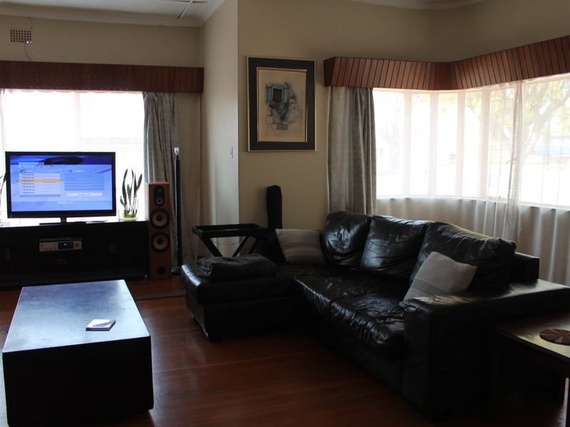 A living room featuring hardwood flooring, a large bay window with timber pelmets, and classic cornice detailing.