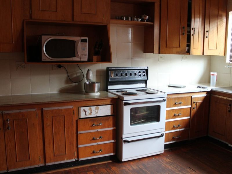 A dated kitchen featuring traditional wooden cabinetry, tiled backsplash, and a freestanding electric stove, offering potential for a modern renovation.