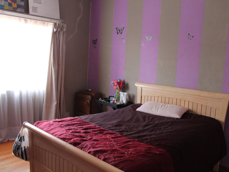 A bedroom featuring timber flooring and striped wall finishes, requiring cosmetic updates to improve the overall condition and aesthetic appeal.