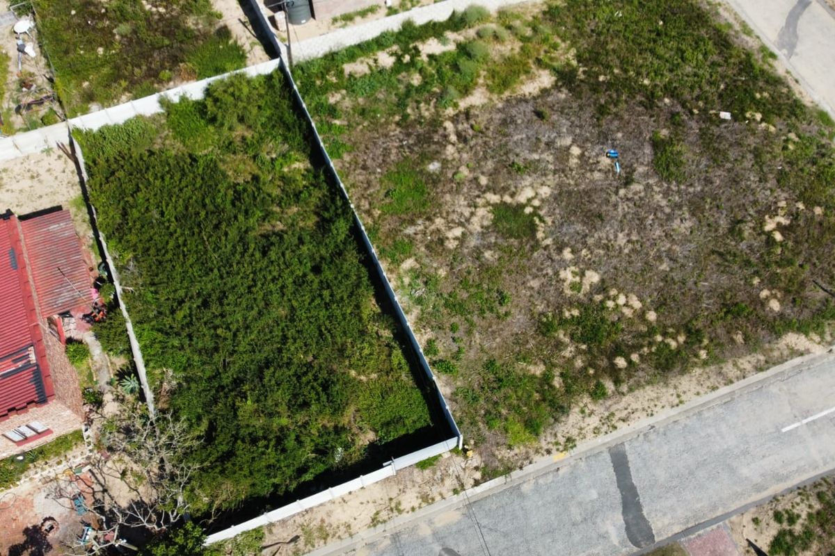 Aerial view of a vacant residential plot featuring perimeter fencing and direct street access, currently covered in natural vegetation.