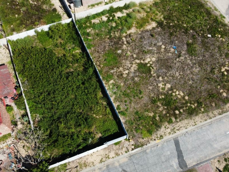 Aerial view of a vacant residential plot featuring perimeter fencing and direct street access, currently covered in natural vegetation.