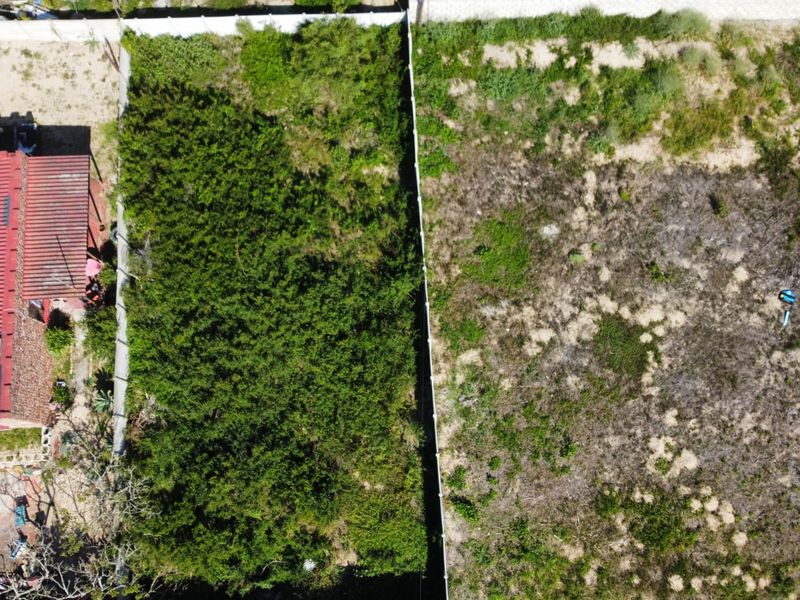 An aerial view of a vacant residential plot featuring boundary fencing and significant natural vegetation cover.