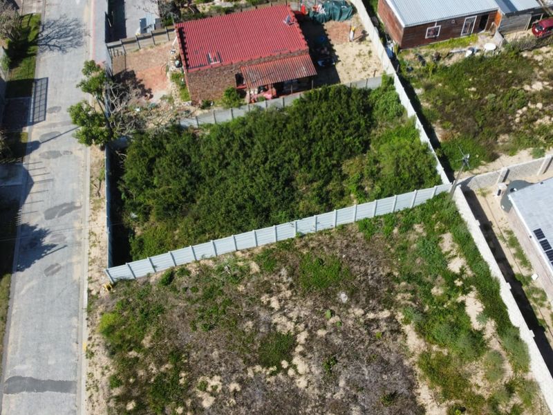 Aerial view of a vacant residential plot featuring perimeter fencing and significant overgrown vegetation, situated in an established neighborhood.