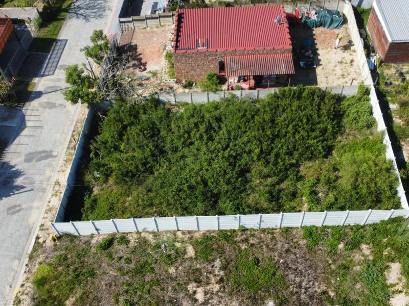 Aerial view of a vacant residential plot enclosed by a precast concrete boundary wall, featuring dense overgrown vegetation.