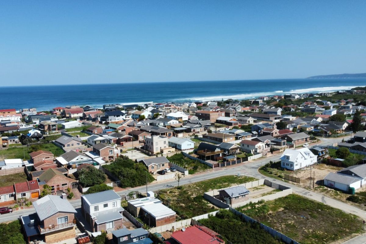 An aerial view of a coastal residential neighborhood featuring established homes, vacant plots, and proximity to the ocean.