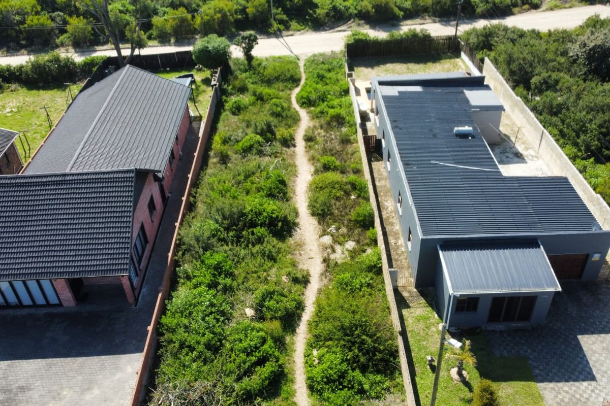 Aerial view of a residential plot featuring a central vacant strip of land flanked by two modern homes with paved driveways and metal roofing.