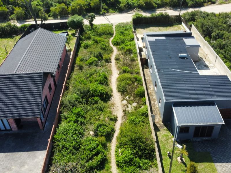 Aerial view of a residential plot featuring a central vacant strip of land flanked by two modern homes with paved driveways and metal roofing.