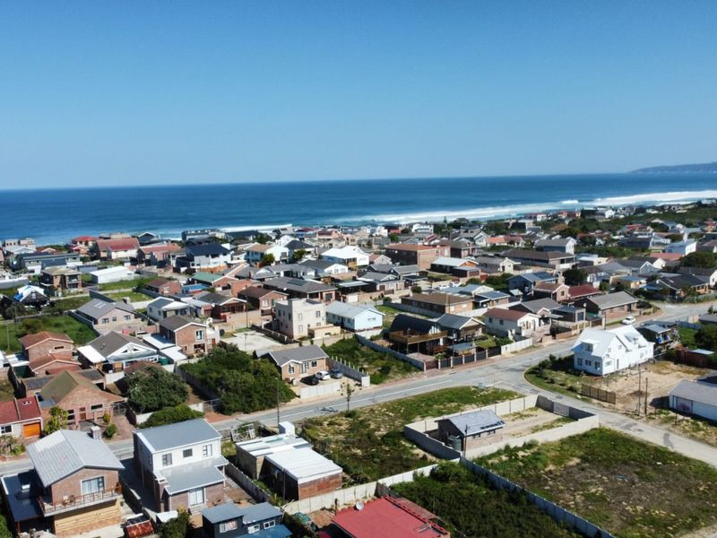 An aerial view of a coastal residential neighborhood featuring established homes, vacant plots, and proximity to the ocean.