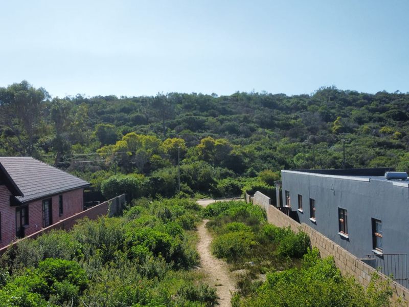 Aerial view of a vacant residential plot situated between two existing properties, featuring natural vegetation and established boundary walls.