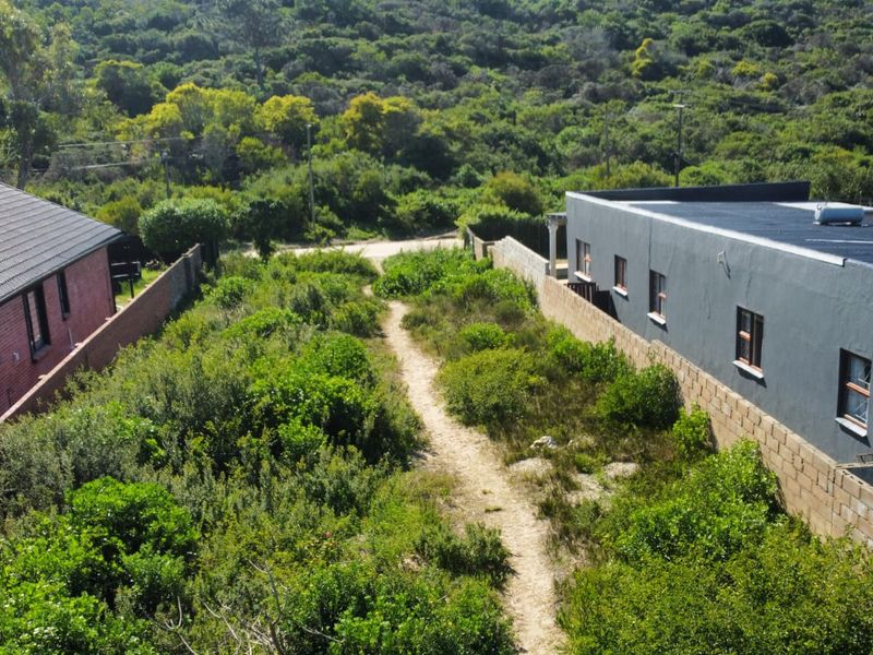 Aerial view of a vacant residential plot situated between two existing properties, featuring natural vegetation and boundary walls.