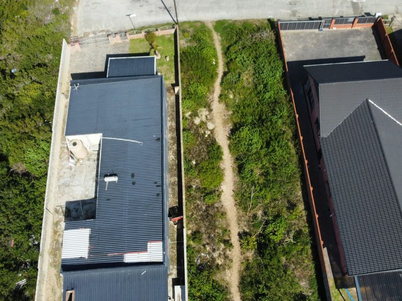 Aerial view of a residential property showing the roof structure, water tank, and adjacent vacant land with natural vegetation.