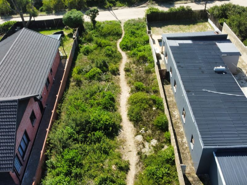 Aerial view of a vacant residential plot situated between two existing properties, featuring natural vegetation and boundary fencing.