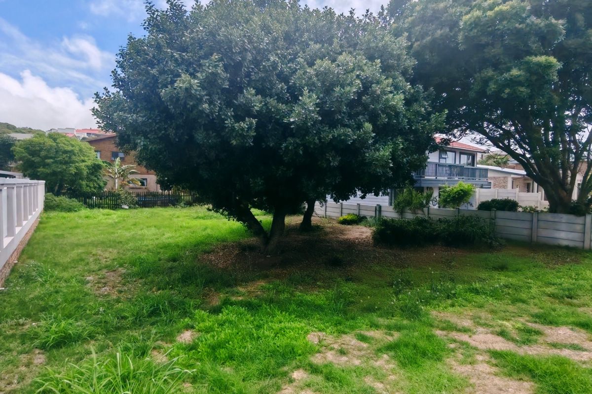 A spacious residential garden area featuring mature trees, established lawn, and secure precast concrete boundary walling.