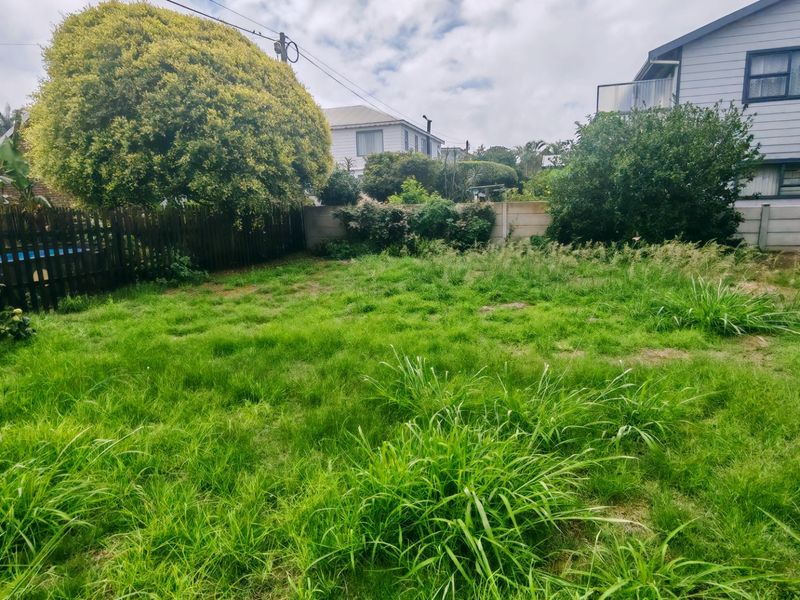 A residential backyard featuring an overgrown lawn, enclosed by a timber fence and precast concrete boundary walls.