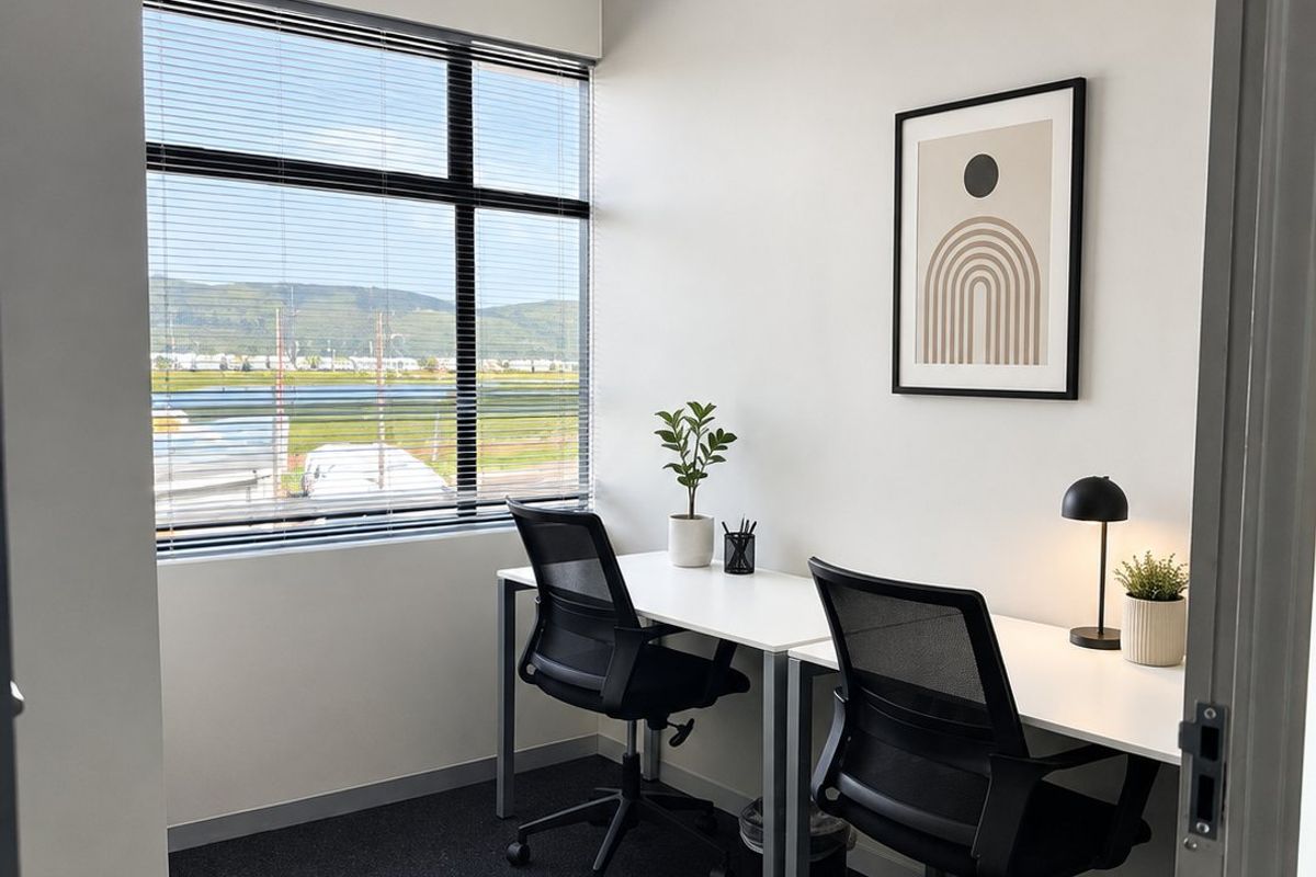 A modern, well-lit office space featuring large windows with venetian blinds, neutral walls, and dark carpeting, suitable for a professional work environment.