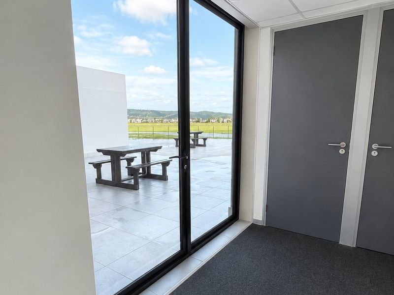 A modern office interior featuring grey doors and carpeted flooring, with direct access to a tiled patio area offering scenic landscape views.